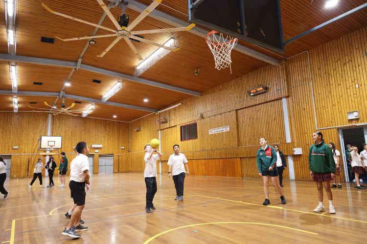 Students in a large school hall playing basketball.