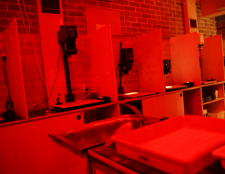 A darkroom illuminated by red lights, showing various photography developing equipment.