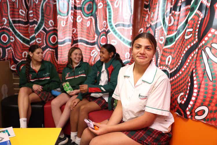 A group of girls sitting on backless lounges with an Aboriginal-designed curtain in the background.