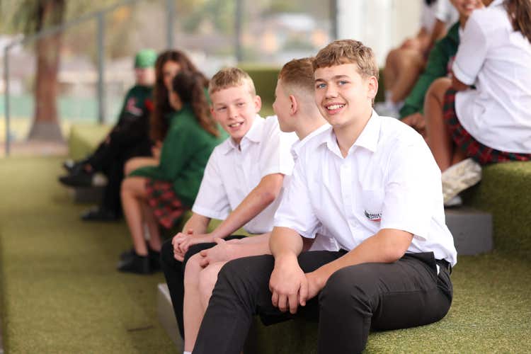 Students sitting on green stairs, chatting in groups, with one boy looking at the camera and smiling.