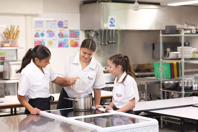 Three girls cooking in a saucepan on a stovetop.