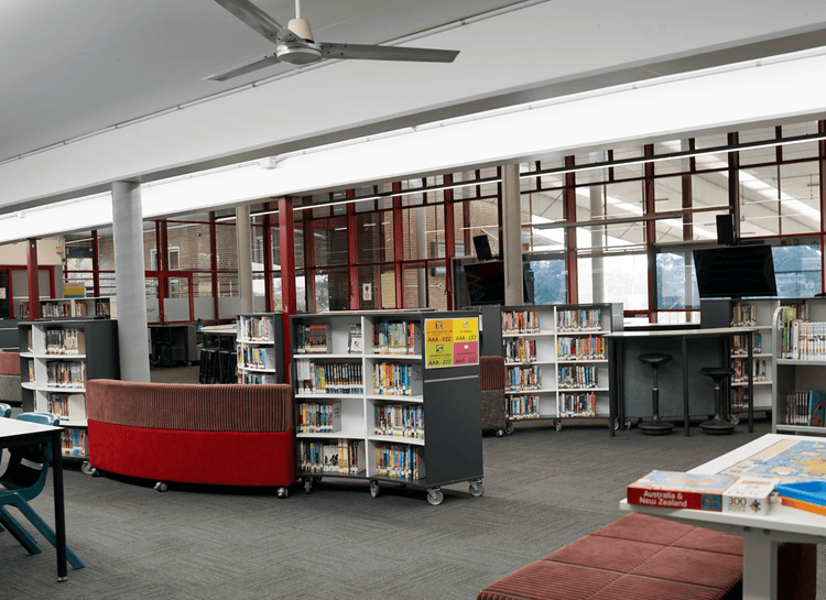 Side view of the library showing curved grey bookshelves, with lounges, tables and chairs.