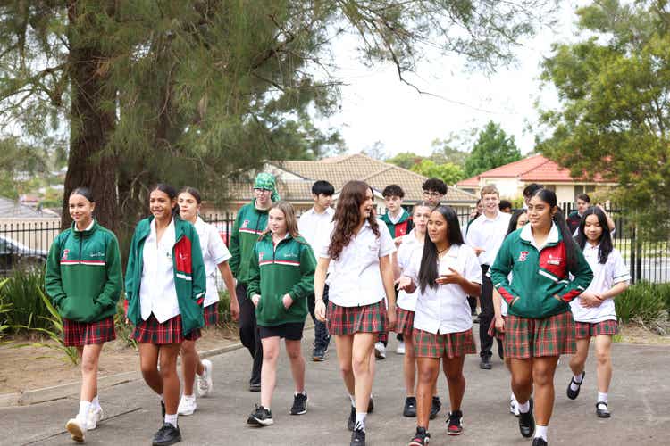 Students in school uniform walking along a footpath lined with lush greenery.