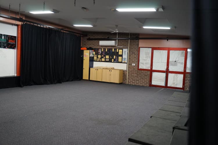 An open carpeted space with black stage curtains and block seating along one side.