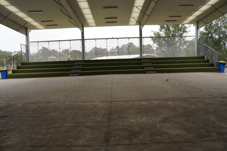 The Library COLA with four levels of green tiered seating, two walkways, and concrete space in front, enclosed by fences on the sides and back, with two bins at the edges.