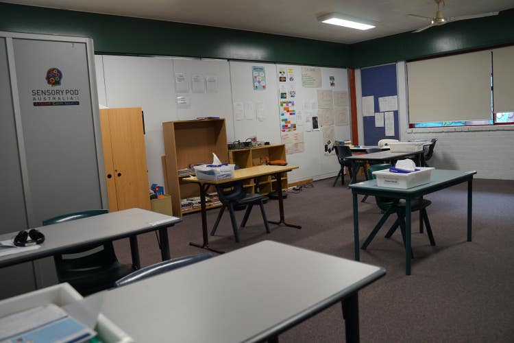A classroom with five large tables spaced apart and a sensory pod at the back.
