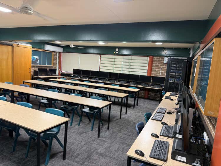 A room with computers along the walls and rows of tables and chairs in the centre.