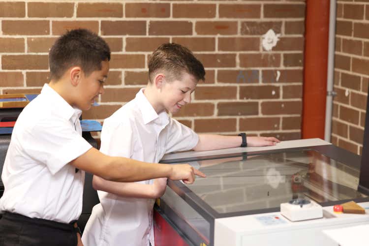 Two boys looking through the glass of a laser cutting machine.