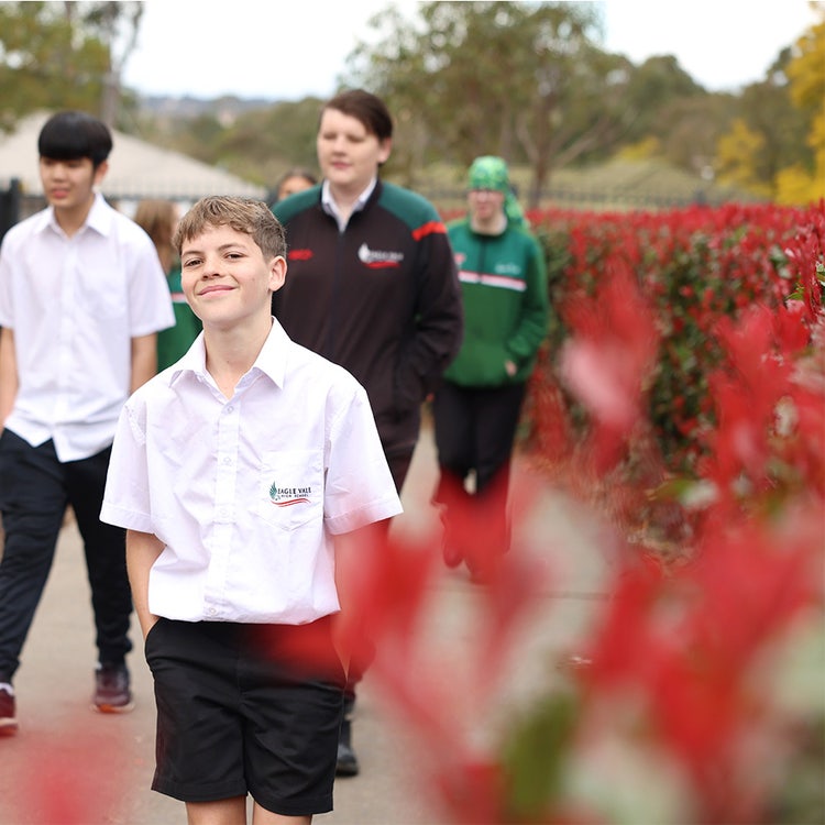 EVHS male student smiling at the camera while walking along a footpath with other students and greenery.